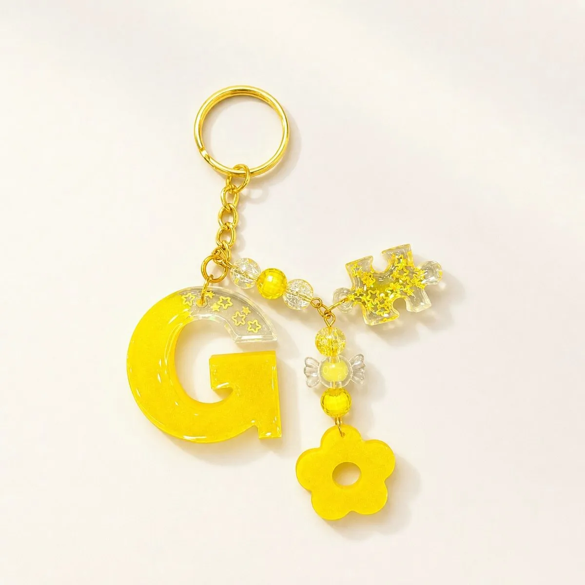 A yellow letter G keychain with gold star confetti, a candy bead and a flower charm