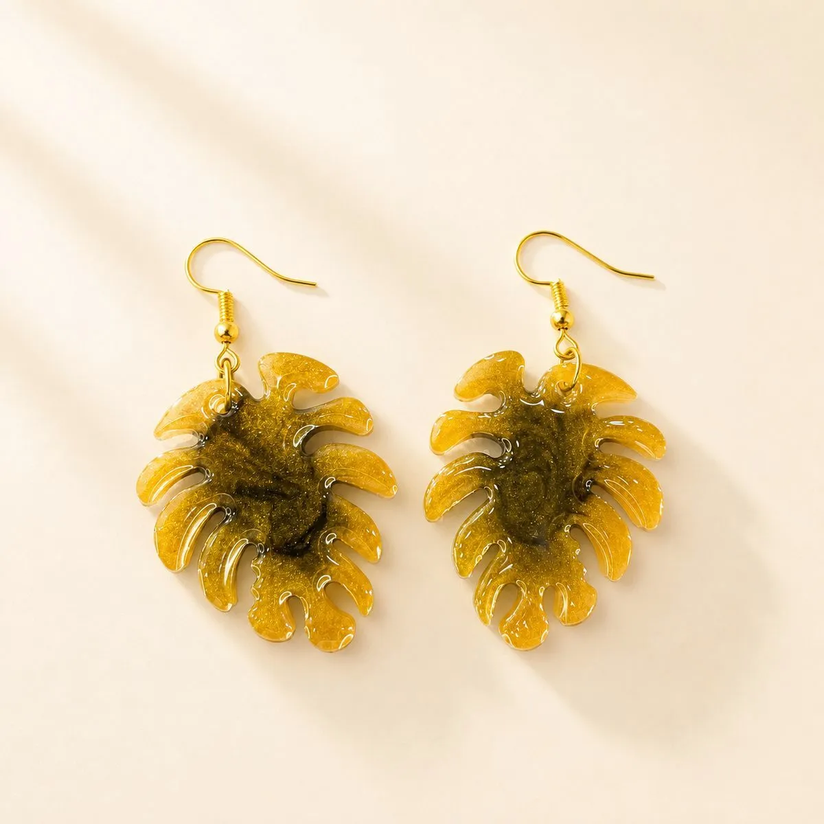 Monstera leaf drop earrings in olive gold with dark green marbling at the centre