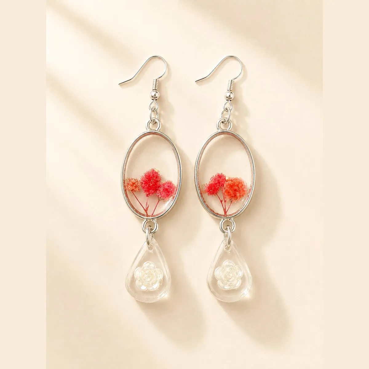 Two-tier drop earrings: a clear oval of small red resin flowers above a teardrop holding a white rose