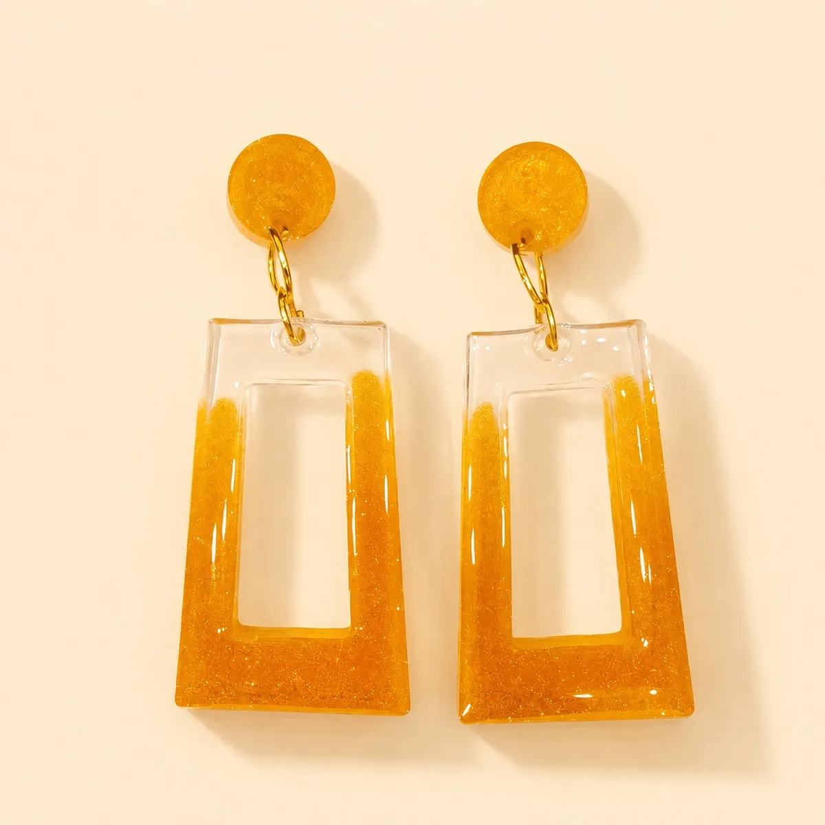 Round amber glitter stud above a large open tapered rectangle, clear at the top running into dense amber glitter
