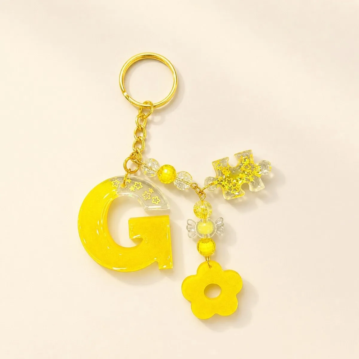 Glossy yellow letter G keychain with gold star confetti, a candy bead and a flower charm