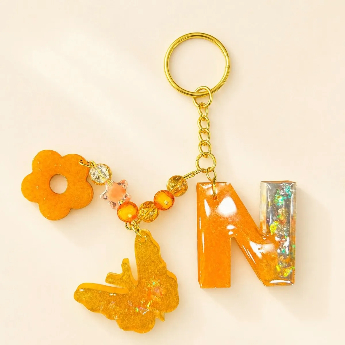 Glossy orange letter N keychain with a holographic glitter bar and a glitter butterfly charm