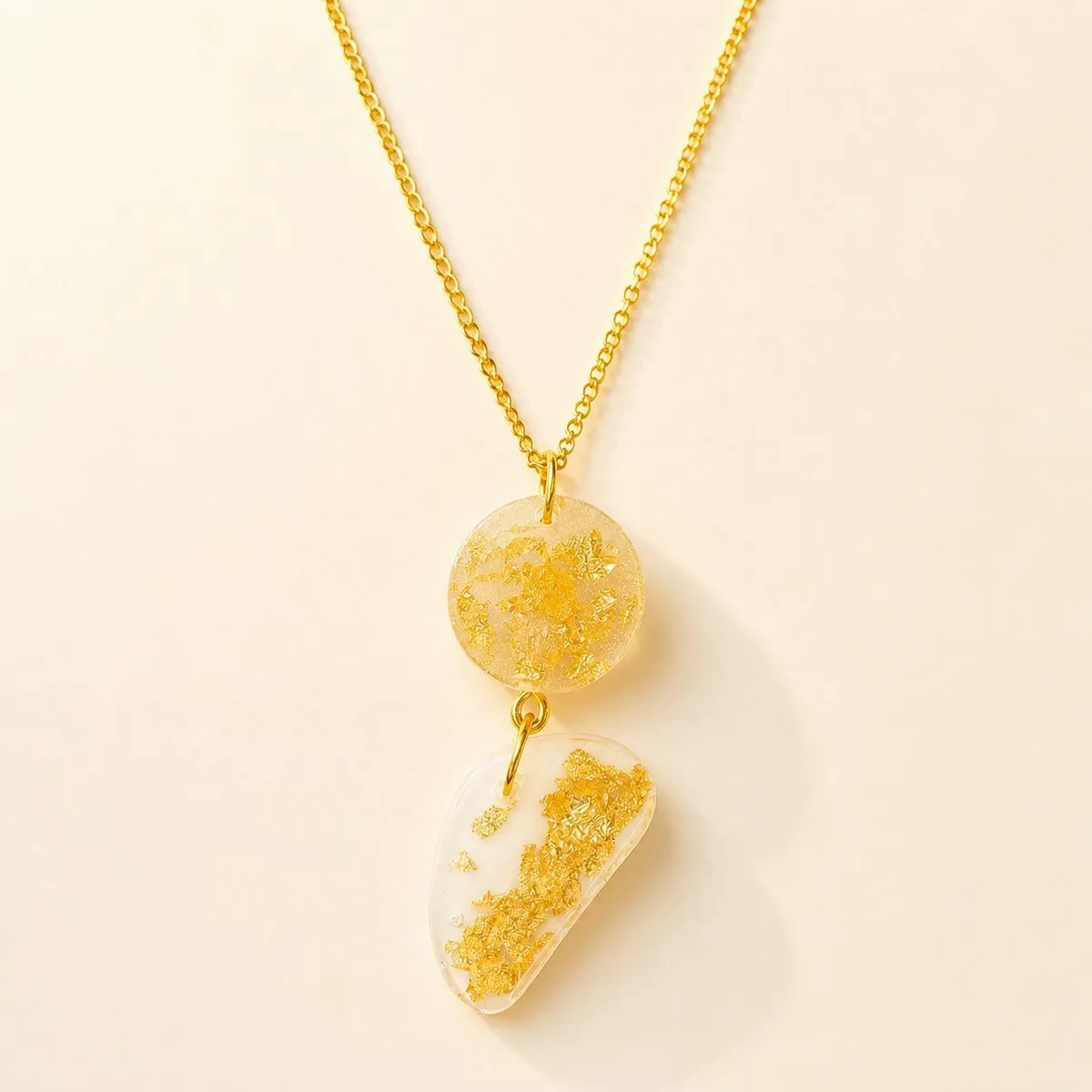 Gold curb chain with a small gold-leaf disc above a cream pebble pendant