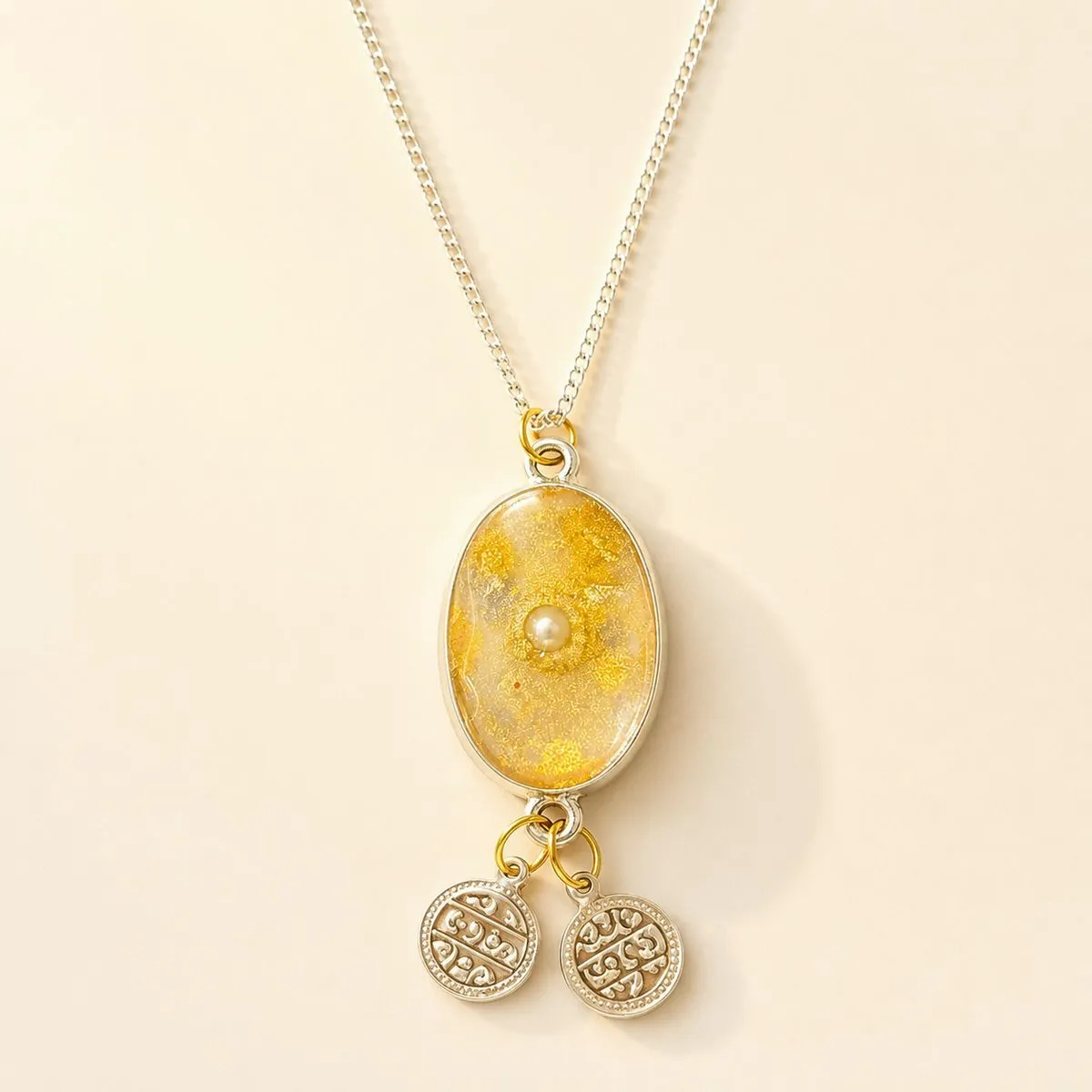 Silver chain with a pale gold shimmer oval, a centre pearl and two engraved coin charms