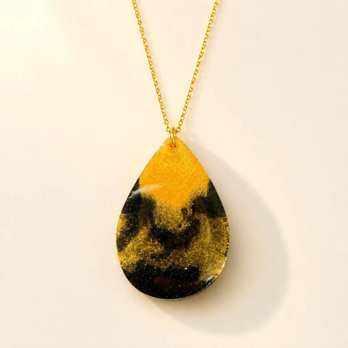 Large teardrop pendant, mustard gold at the top flowing into black with gold glitter marbling